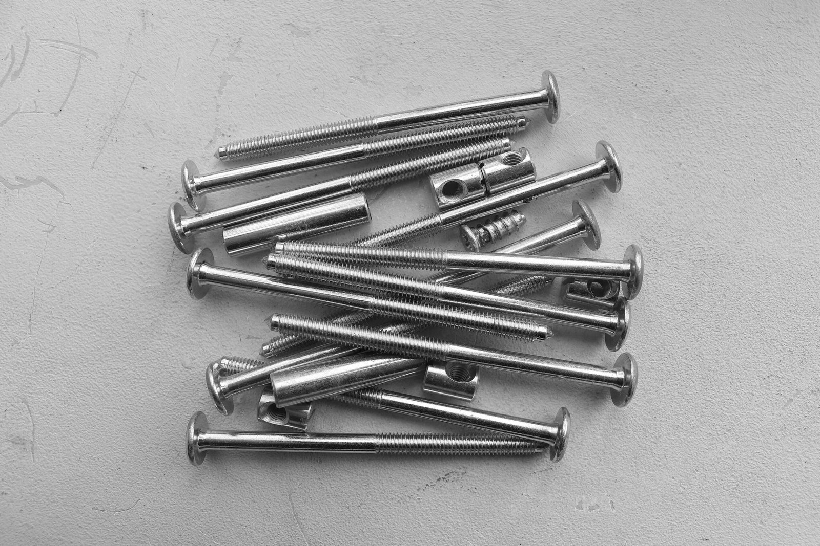 A collection of metal screws and bolts arranged on a textured white surface.